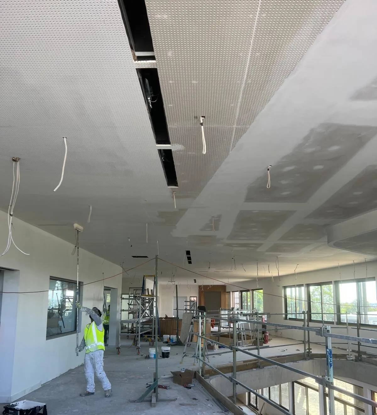 A painter rolling a perforated ceiling over dried plaster patches
