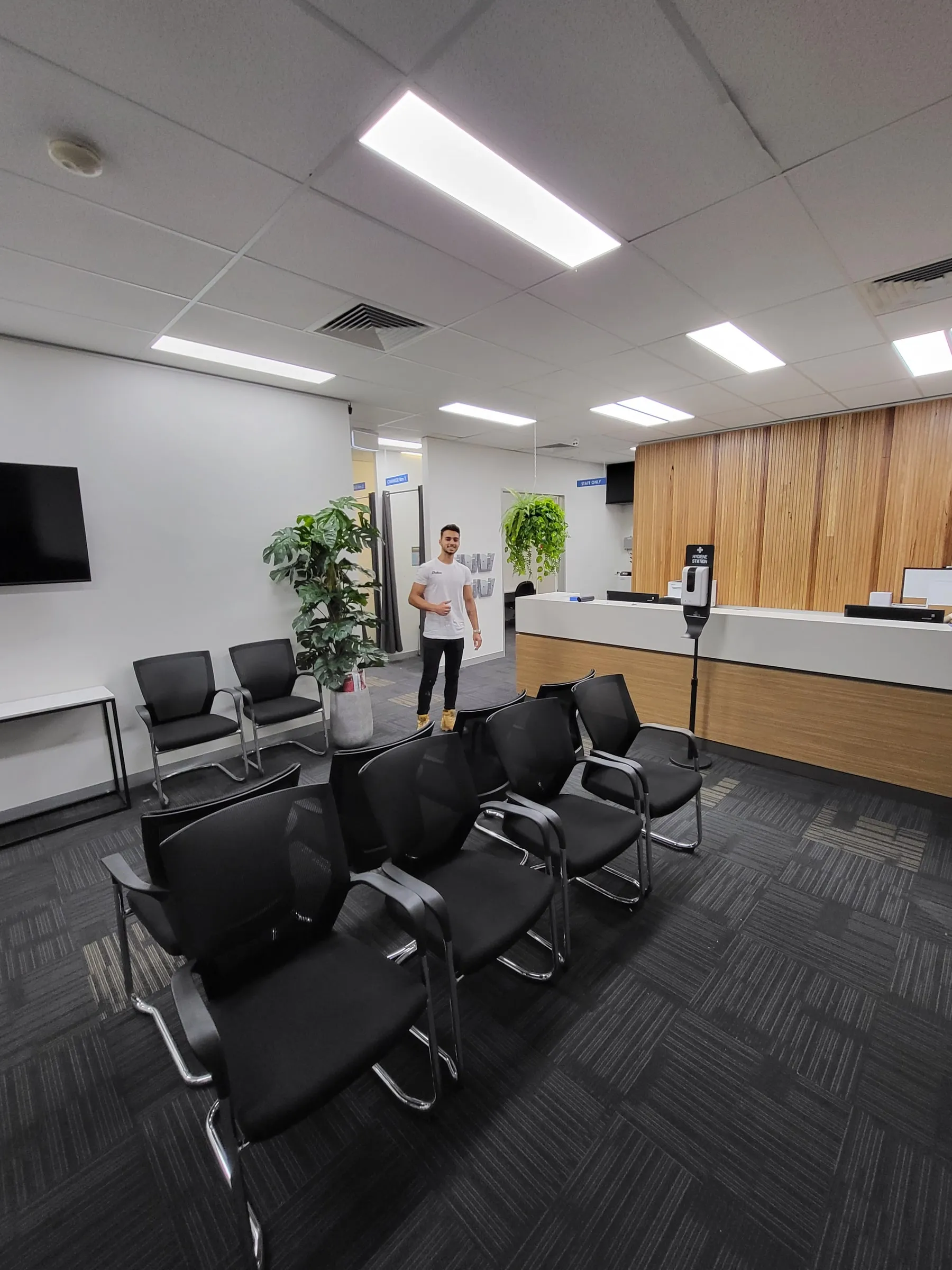 A clinic waiting room with black chairs and a wood reception desk