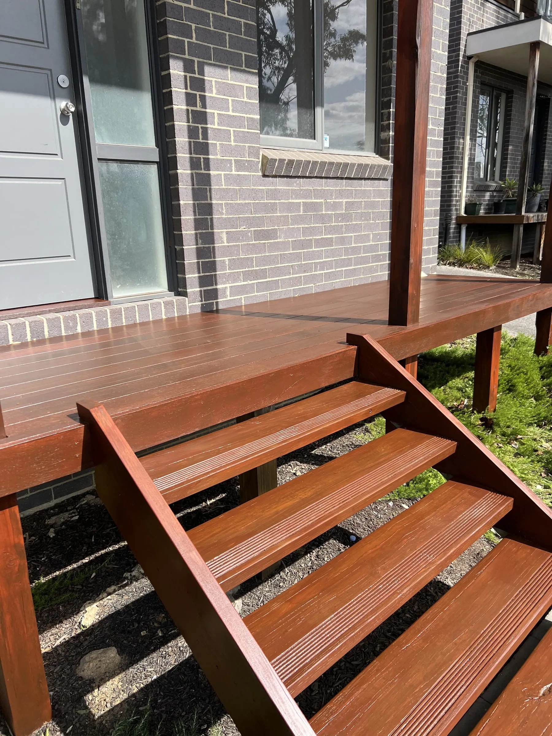 Stained wood deck stairs at the back of a brick house