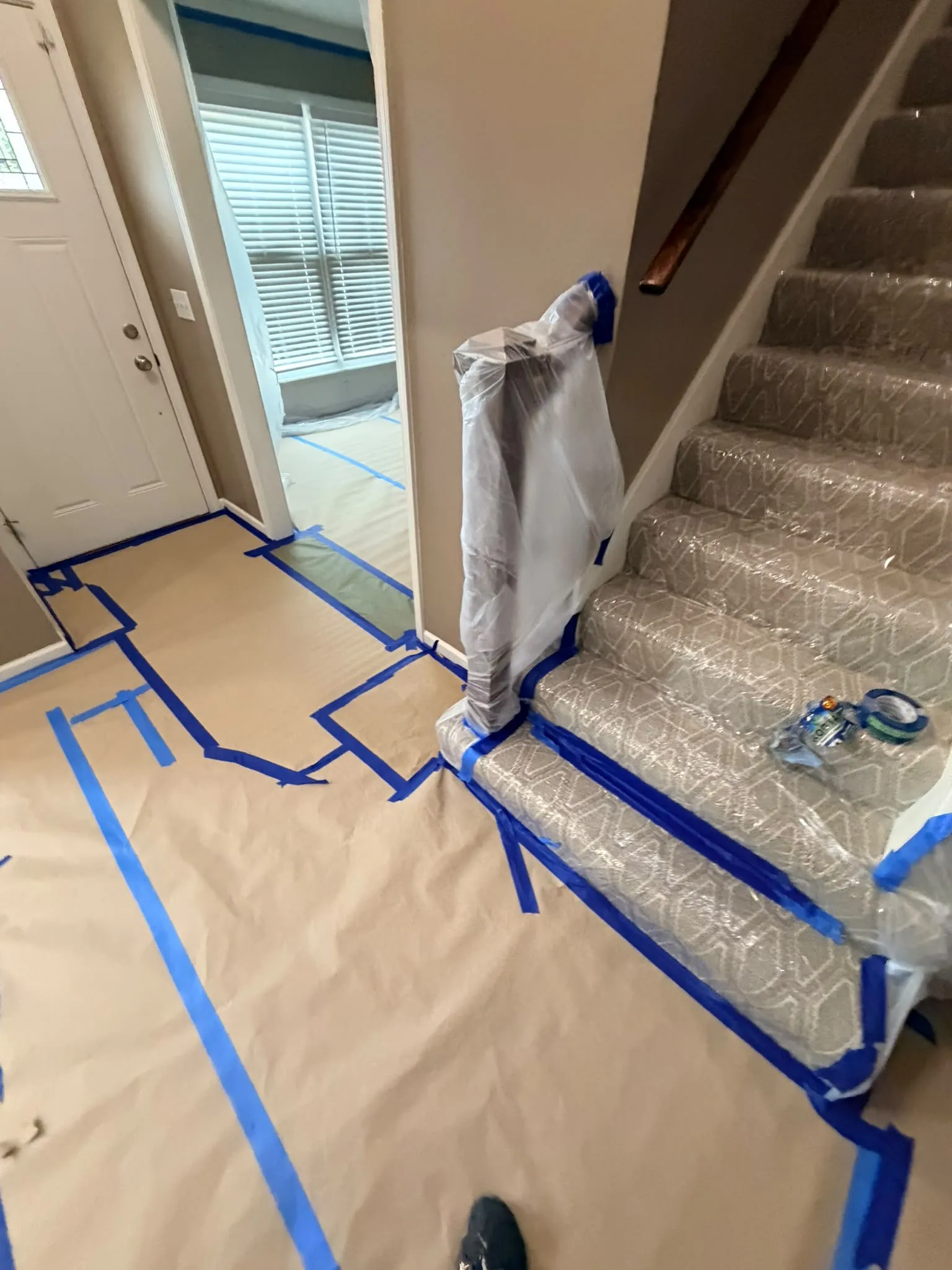 An entry hall with the stairs wrapped in plastic and the floor covered in paper