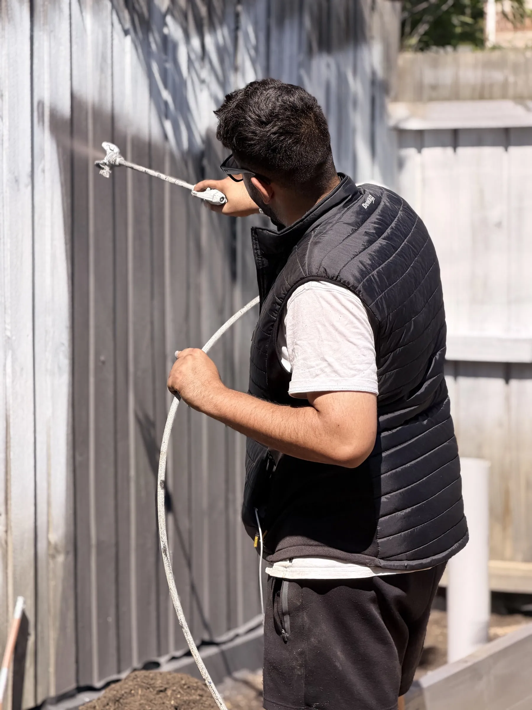 A painter spraying a wood privacy fence