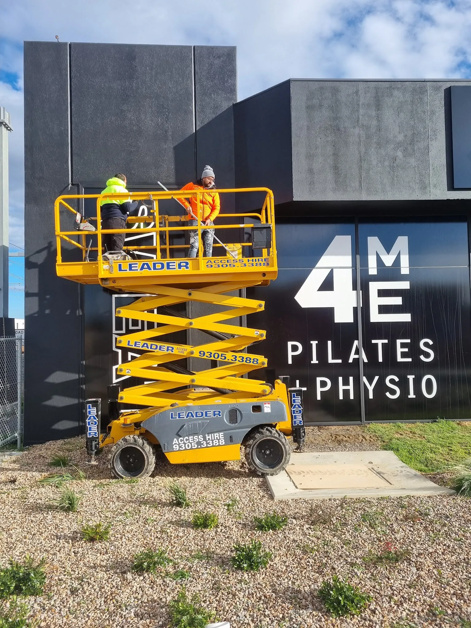 A painter on a scissor lift at a pilates studio sign wall