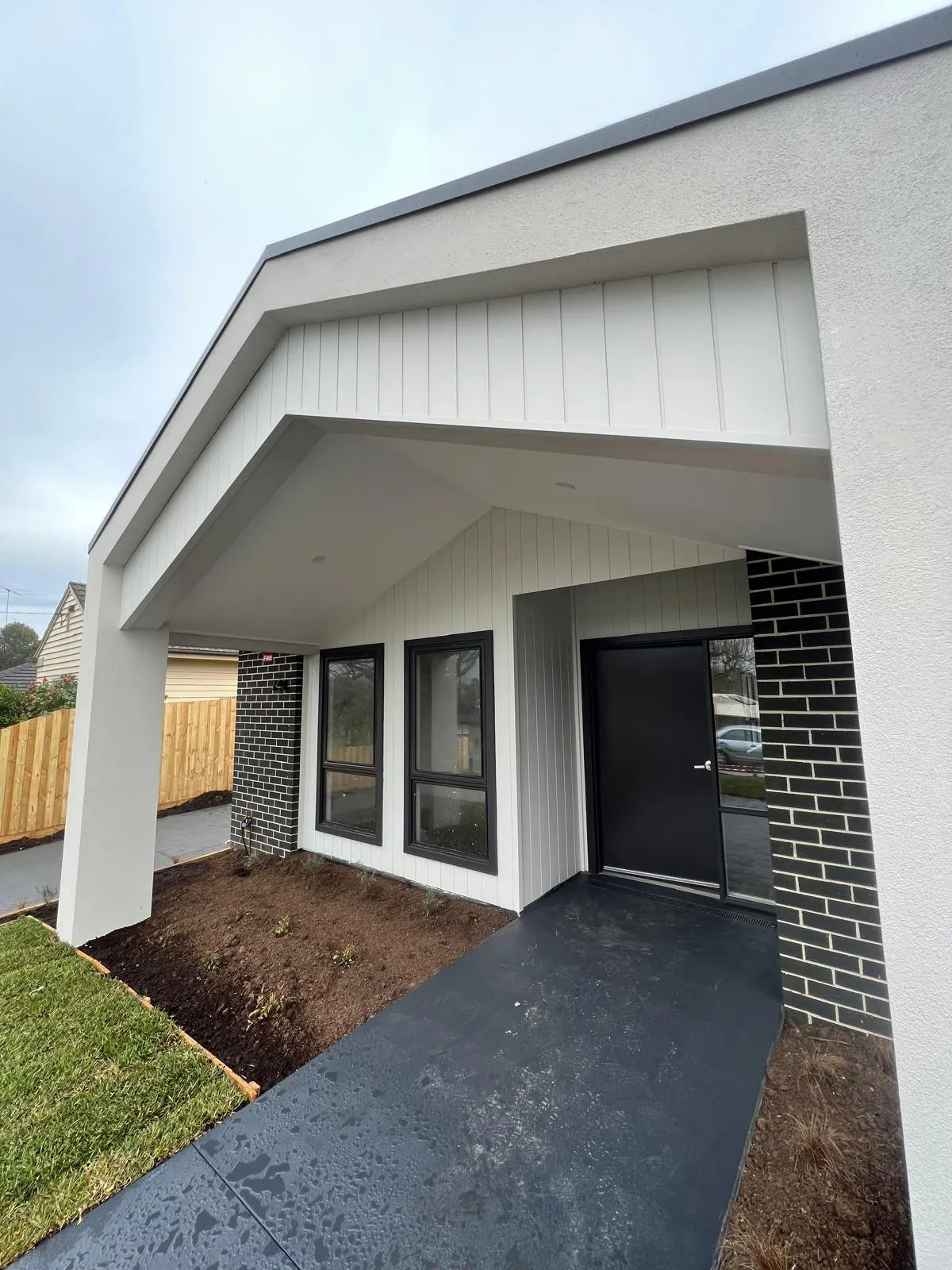 A new house porch with white stucco, vertical siding and black window frames