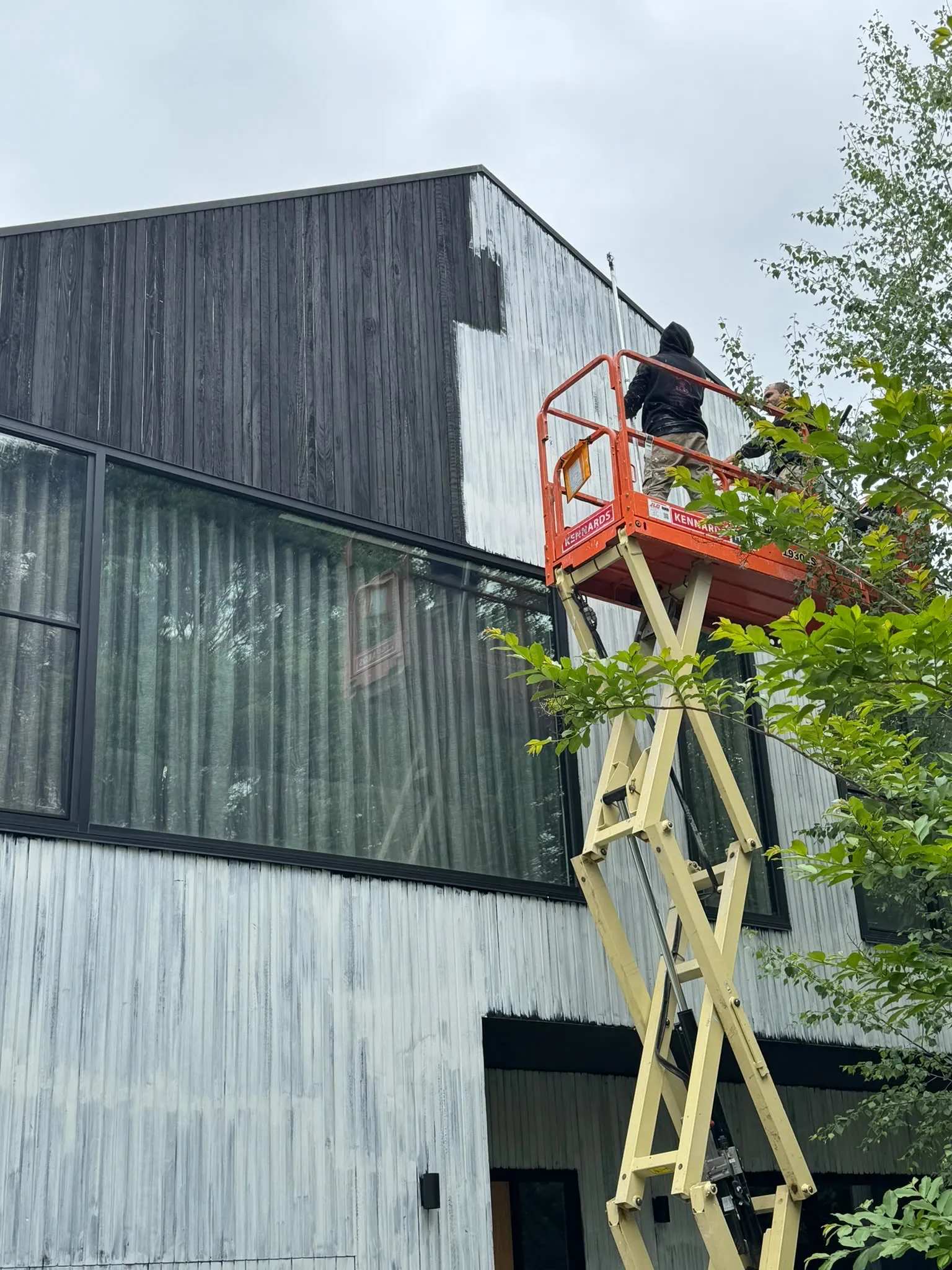 A painter on a scissor lift at a two-story house with wood siding