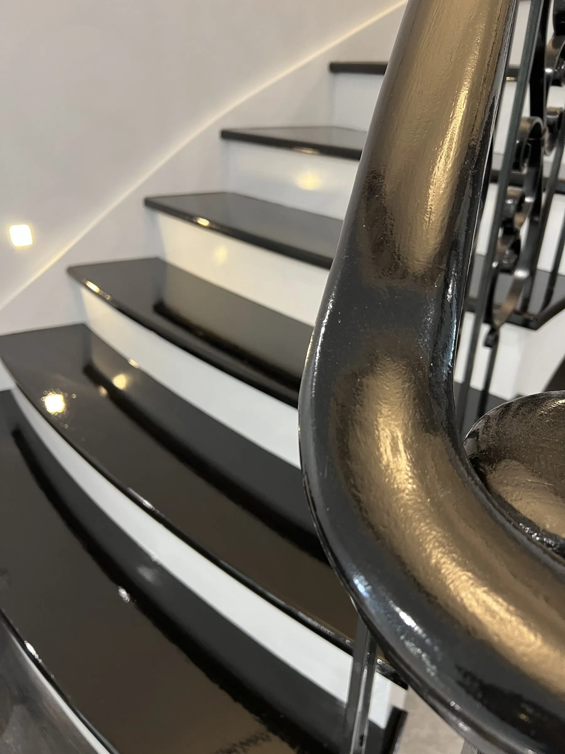 A curved staircase with gloss black treads, white risers and a black handrail