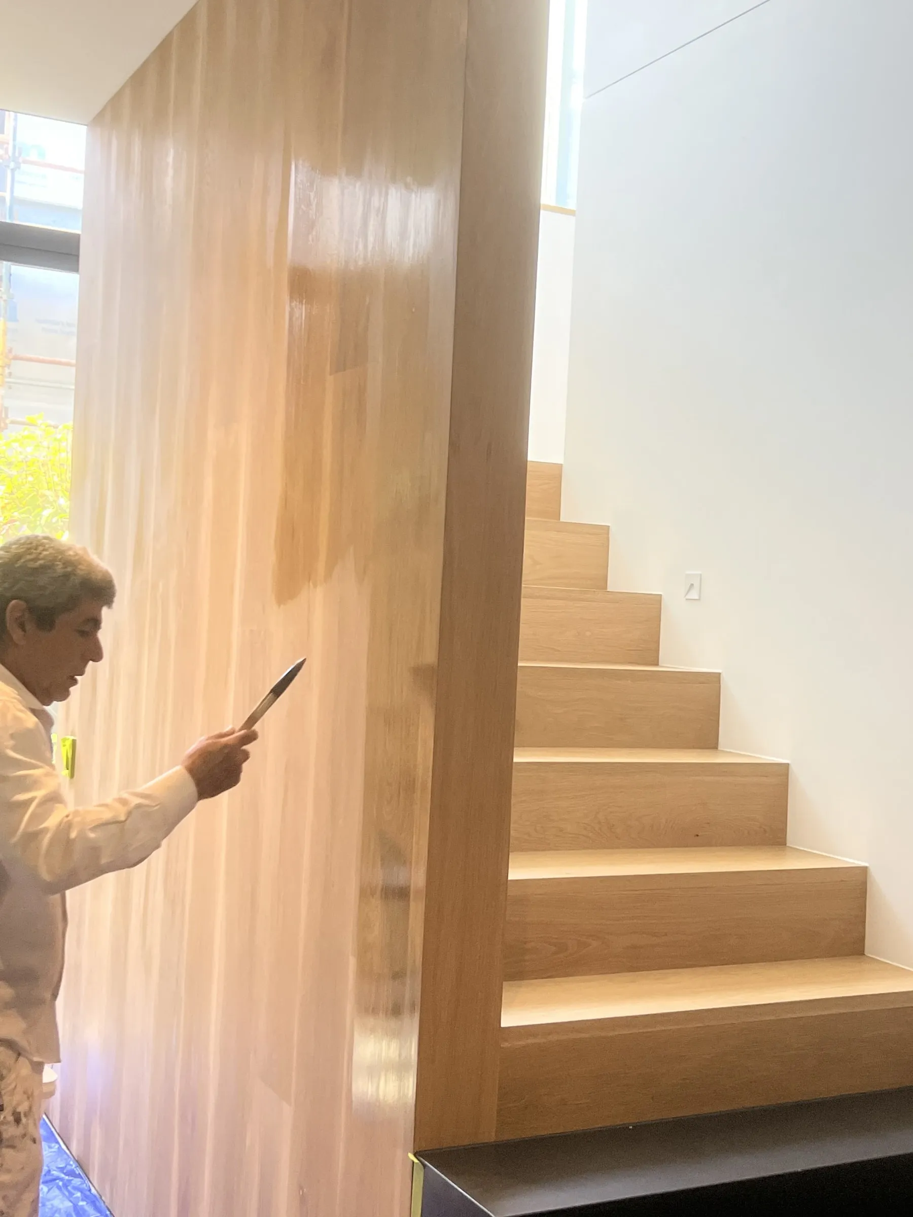 A painter brushing finish onto a wood feature wall beside oak stairs