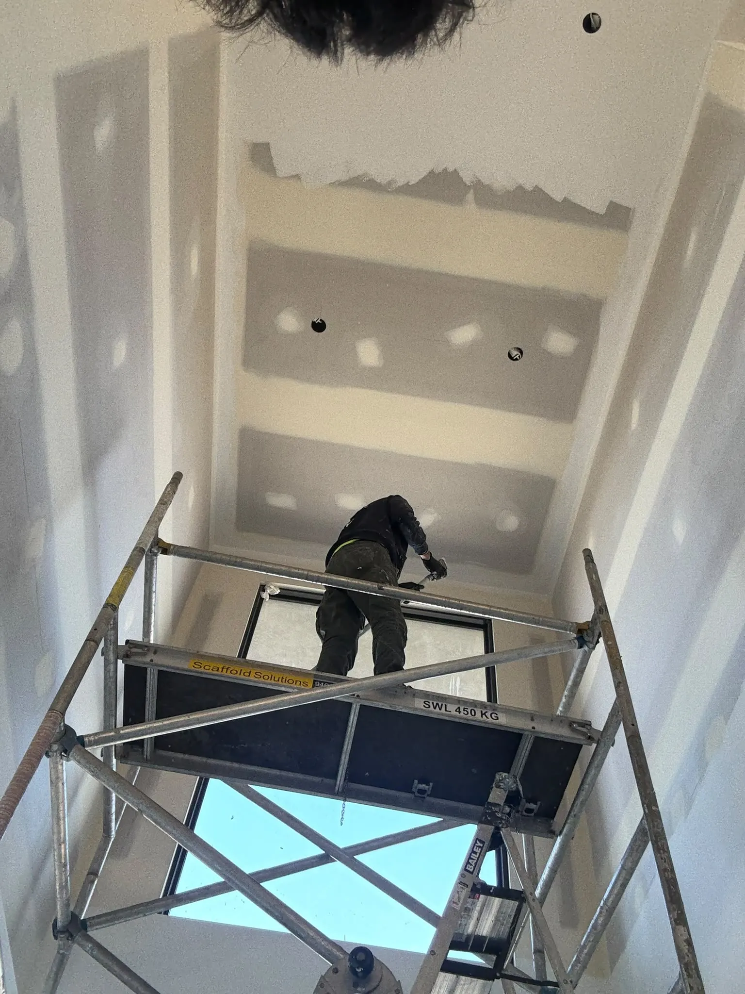 A plasterer on a rolling scaffold finishing a stairwell ceiling